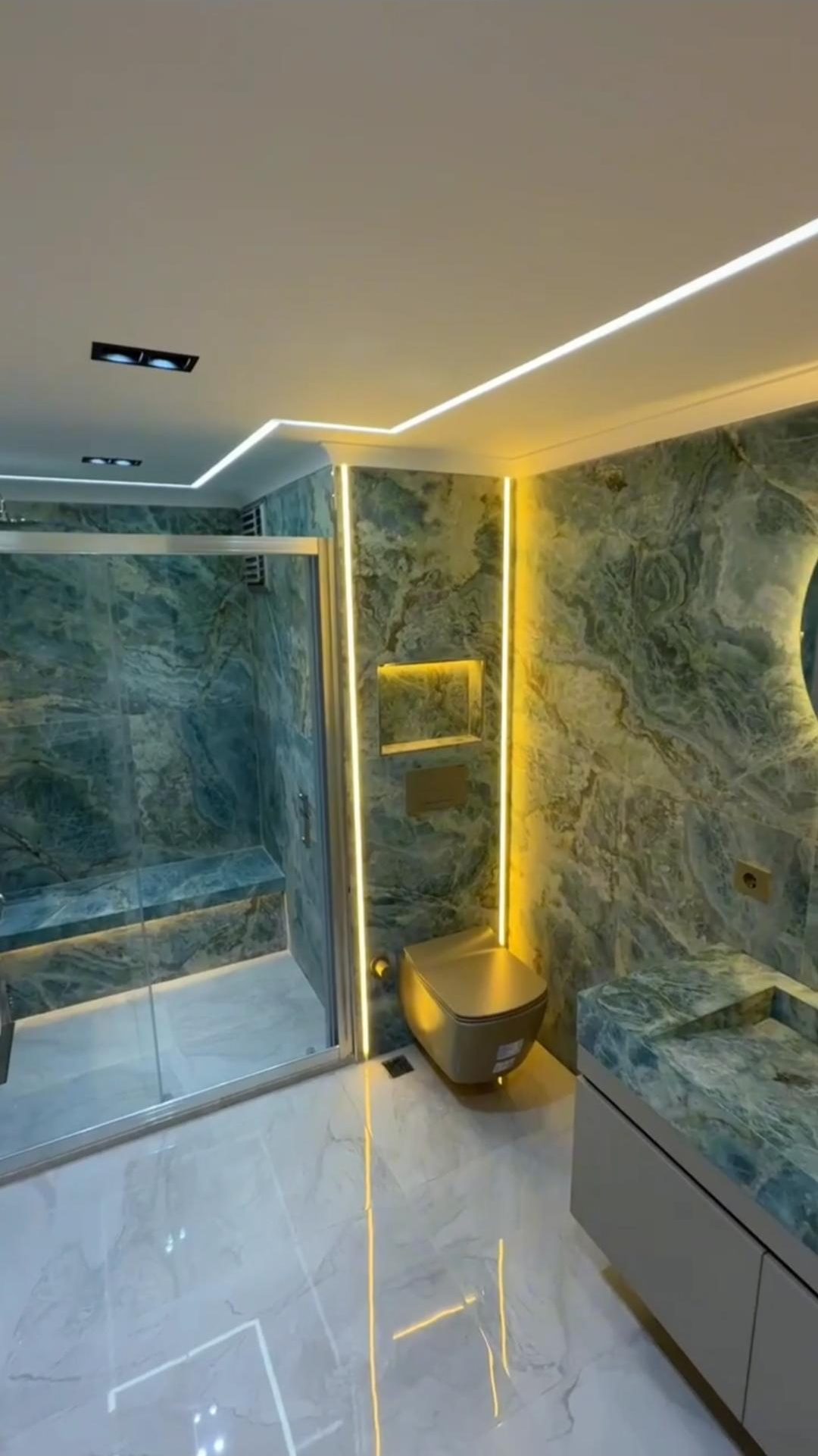 Arkadan aydınlatmalı yeşil oniks kaplı banyo, gizli LED hatları ve altın rengi armatürler